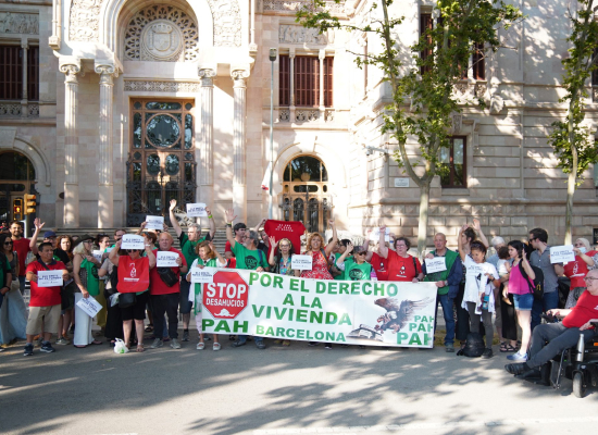 Activistas de la PAH (Plataforma de Afectadas por la Hipoteca) y otros movimientos sociales se concentran frente a un edificio institucional de Barcelona. Sostienen una pancarta que reclama “Por el derecho a la vivienda” y carteles de “Stop Desahucios”